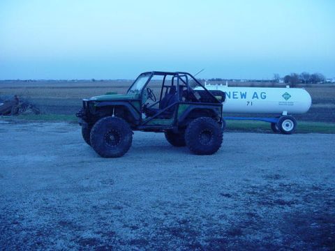 1992 Ford Bronco - A modified off-road vehicle is parked next to a large white tank trailer in a rural setting.