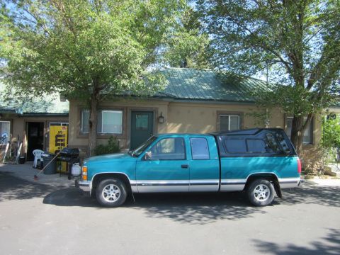 1991 Ford LTD Crown Victoria - A teal pickup truck with a black camper shell is parked in front of a building on a sunny day.