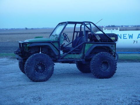 1992 Ford Bronco - A modified 1992 Ford Bronco sits on a gravel lot with a large white tank in the background.