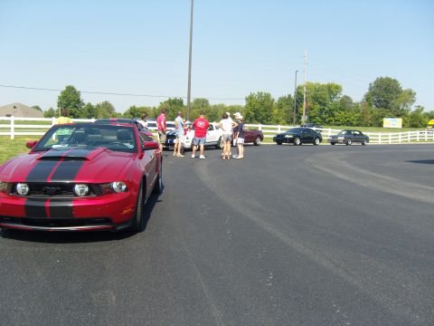 2007 Ford Mustang - A group of people stand around several cars parked in an asphalt lot on a sunny day.