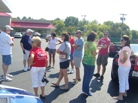 2007 Ford Mustang - A group of people gathered around a red 2007 Ford Mustang at a car show.