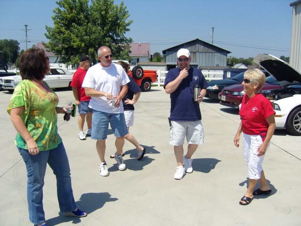 People standing on pavement near several cars, some with hoods open