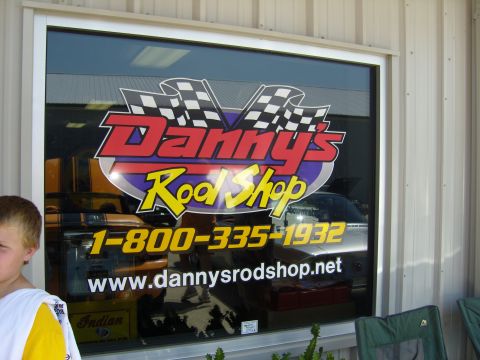 2007 Ford Mustang - The storefront window of Danny's Rod Shop displays their logo, contact information, and reflections of vehicles within the shop.