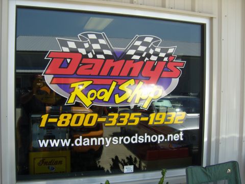 2007 Ford Mustang - A window displays the "Danny's Rod Shop" logo, phone number, and website, with reflections of cars and a person visible.