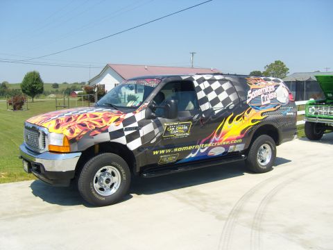 2007 Ford Mustang - A custom-wrapped Ford Excursion, likely from a car show, is parked next to a green Ford Bronco.