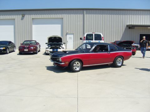 2007 Ford Mustang - Several cars are parked outside a warehouse, including a red and black coupe in the foreground.