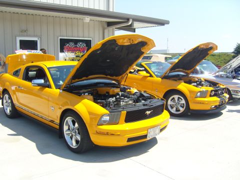 2007 Ford Mustang - Two yellow Ford Mustangs are parked outside a building with their hoods open, displaying their engines.