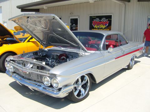 2007 Ford Mustang - A silver 1961 Chevrolet Impala is displayed with its hood open, revealing the engine, next to a yellow Ford Mustang.