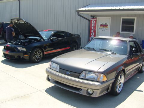2007 Ford Mustang - Two Ford Mustangs are parked outside a building. One is a gray fox body, the other is a black Shelby GT500.