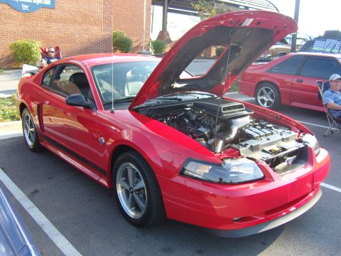 2007 Ford Mustang - Red Ford Mustang with hood open at a car show, another Mustang visible in background.