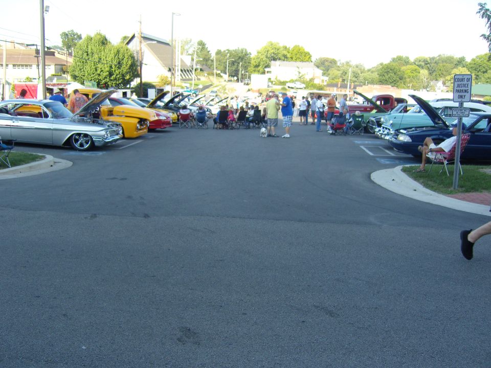 Cars parked in a lot with people around, some hoods are up. A sign says 'Court of Justice Parking Only'