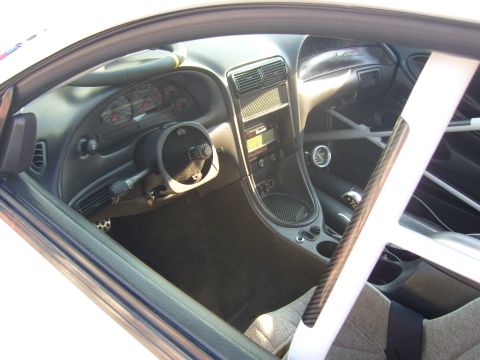 2007 Ford Mustang - Interior of a modified sports car or track car with a small aftermarket steering wheel, carbon fiber trim on the door sill, roll cage bar,…