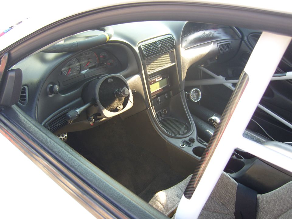 Race car interior showing aftermarket steering wheel, roll cage bar, and modified dashboard