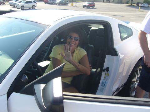 2007 Ford Mustang - A woman waves from the driver's seat of a white Ford Mustang, parked outdoors.