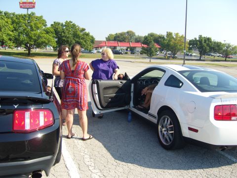 2007 Ford Mustang - Two Mustangs are parked in a lot, one white and one black, with people gathered around.