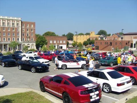 2007 Ford Mustang - A gathering of Ford Mustangs in a parking lot on a sunny day, with several people socializing.