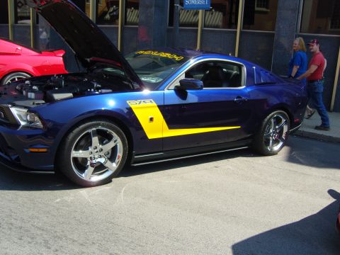 2007 Ford Mustang - A blue 2007 Ford Mustang with a yellow stripe and ROUSH decal is parked with its hood open at a car show.