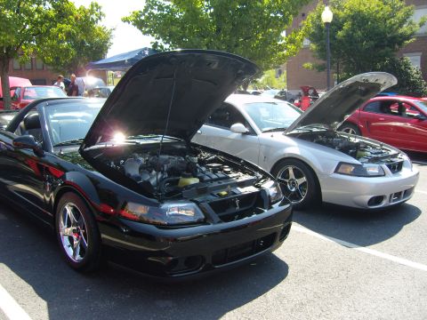 2007 Ford Mustang - Two Mustangs, a black convertible and a silver coupe, are parked with their hoods open at an outdoor car show.