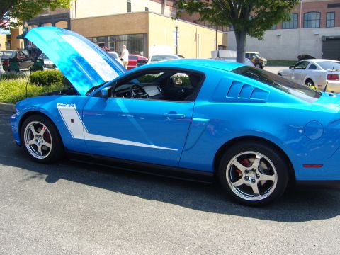 2007 Ford Mustang - A blue Ford Mustang with racing stripes and louvers on the rear window is parked outside with its hood open.