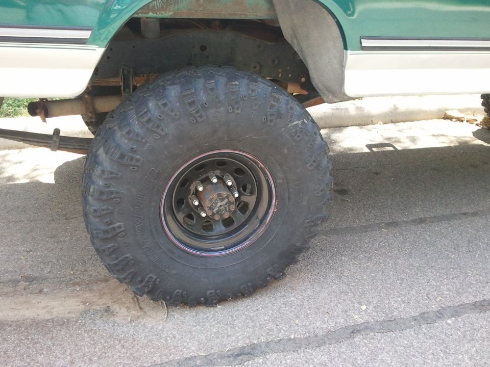 Close-up of a large off-road tire on a truck's suspension, showing leaf springs and frame
