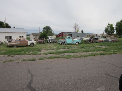1991 Ford LTD Crown Victoria - A collection of weathered vehicles sits in a grassy lot under an overcast sky.