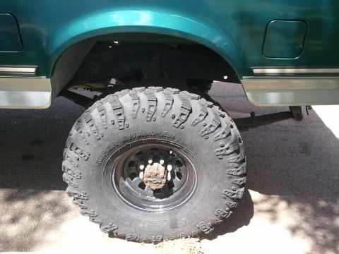 2004 Ford F-350 - Close-up of a truck's rear wheel and fender, showing off-road tires and green paint.