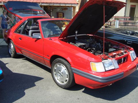 2007 Ford Mustang - A red convertible with its hood open is parked outside a building.