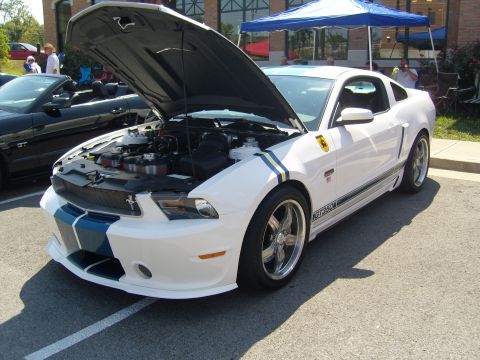 2007 Ford Mustang - A white 2007 Ford Mustang GT350 with racing stripes and its hood open is parked at an outdoor event.