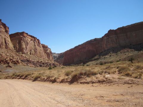 1991 Ford LTD Crown Victoria - Driving through a desert canyon landscape with prominent red rock cliffs and sparse vegetation.