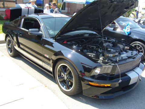 2007 Ford Mustang - A black Shelby GT Mustang is displayed with its hood open, revealing the engine bay. Another car is parked behind it.