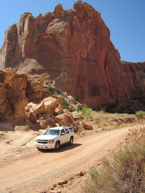 1991 Ford LTD Crown Victoria - A white SUV navigates a dusty road through a scenic desert landscape dominated by towering red rock formations.