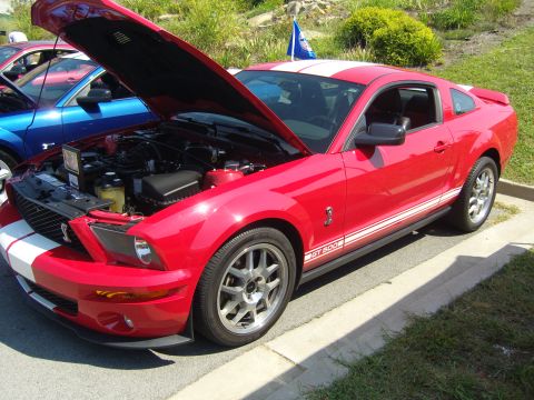 2007 Ford Mustang - A red Ford Mustang GT500 is parked with its hood open, next to a blue Mustang.