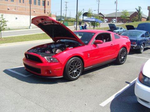 2007 Ford Mustang - A red 2007 Ford Mustang is parked with its hood up, alongside other vehicles at an outdoor event.