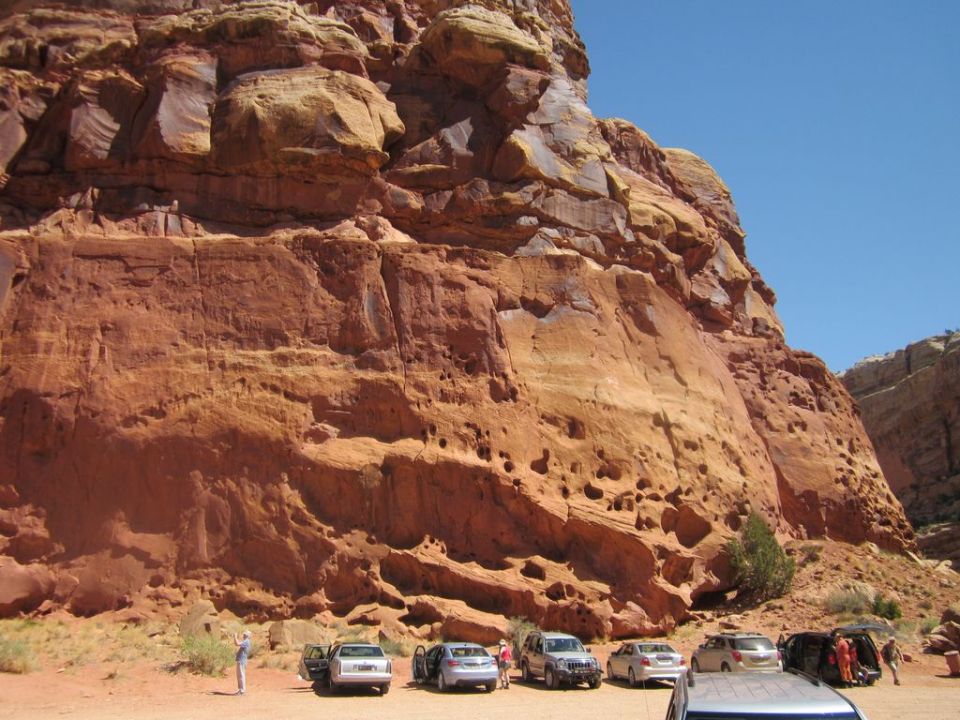 Red rock formations tower over a parking area with several cars