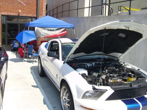 2007 Ford Mustang - A white 2007 Ford Mustang with racing stripes is parked with its hood up, revealing the engine bay.