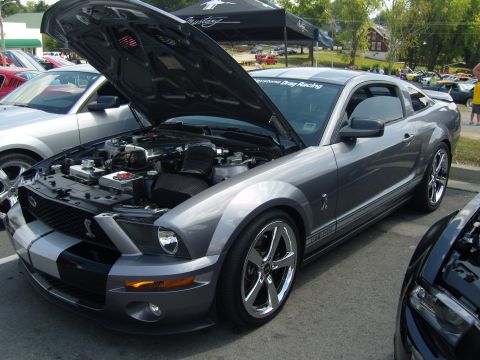 2007 Ford Mustang - Gray Ford Mustang with racing stripes and hood open at a car show.