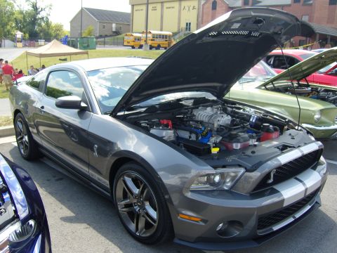 2007 Ford Mustang - A gray Ford Mustang Shelby GT500 is displayed with its hood open, revealing the engine, at an outdoor car show.