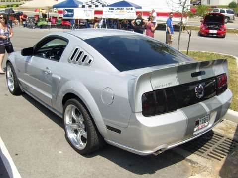 2007 Ford Mustang - A silver 2007 Ford Mustang GT is parked at an outdoor event, showing off its racing stripes and custom wheels.