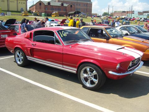 2007 Ford Mustang - A red classic Mustang coupe with white racing stripes is parked at an outdoor car show.