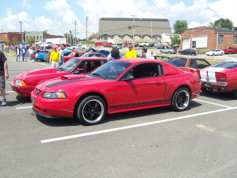 2007 Ford Mustang - Red 2007 Ford Mustang GT with black stripes and wheels at a car show.