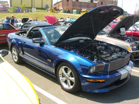 2007 Ford Mustang - A blue 2007 Ford Mustang Shelby GT convertible is parked with its hood open at an outdoor car show.