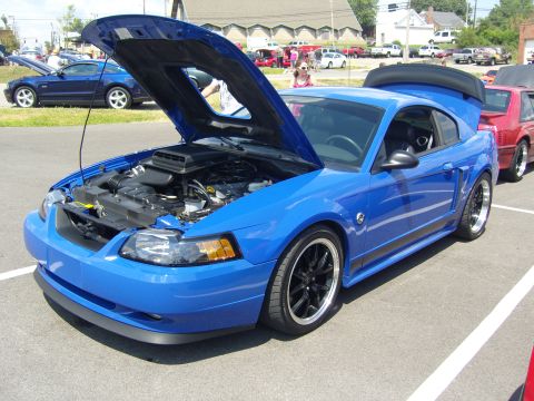 2007 Ford Mustang - A blue Ford Mustang is displayed with its hood open, revealing the engine bay. Other vehicles are visible in the background.