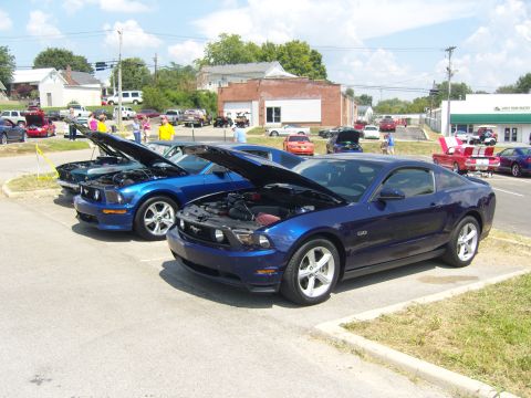 2007 Ford Mustang - Several Ford Mustangs are parked with hoods open at a car show.