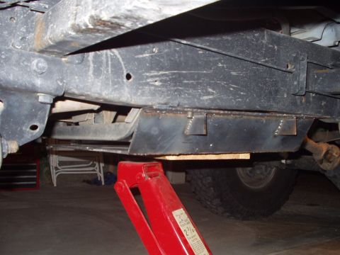 1993 Ford Bronco - Vehicle undercarriage with skid plate and jack support. Tire visible in the background.