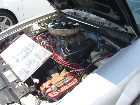 2007 Ford Mustang - The engine bay of a car, a Ford Racing valve cover and an open manual. A second vehicle is partially visible.