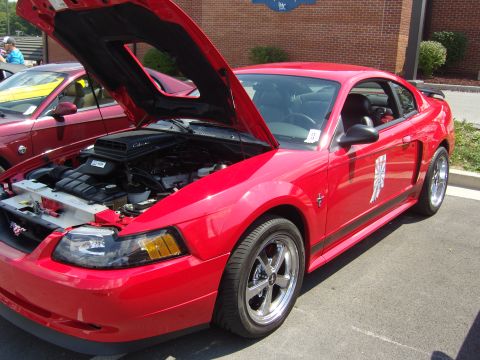 2007 Ford Mustang - A red Ford Mustang Cobra is displayed with its hood open, revealing the engine bay. Another Mustang is visible behind it.