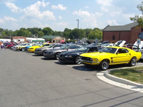 2007 Ford Mustang - A line of cars, including a bright yellow classic Mustang, are parked in a lot on a sunny day.