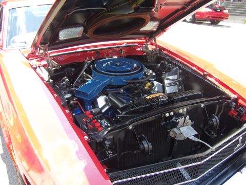 2007 Ford Mustang - The engine compartment of a vintage red car is open, revealing its mechanical components. A second vehicle is visible in the background.