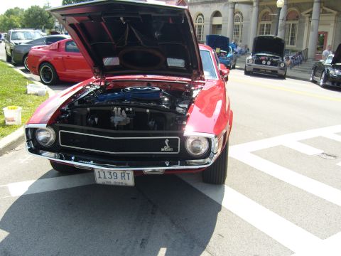 2007 Ford Mustang - A red 1969 Ford Mustang is parked with its hood open, displaying the engine, alongside other vehicles at a car show.