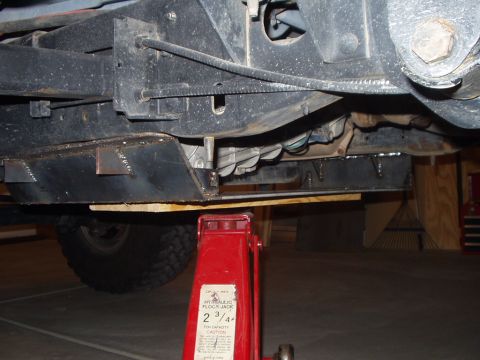 1993 Ford Bronco - The underside of a vehicle is shown, a skid plate and a red hydraulic jack supporting it.